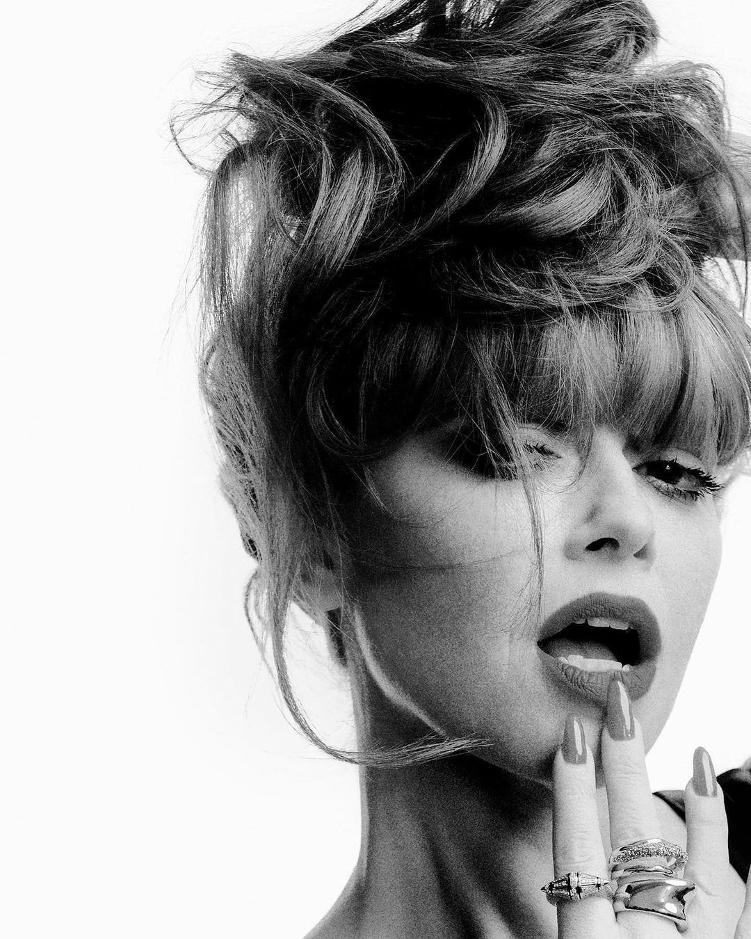 Monochrome portrait of woman with styled hair, light makeup, and several rings posing in a photo studio with a white background.