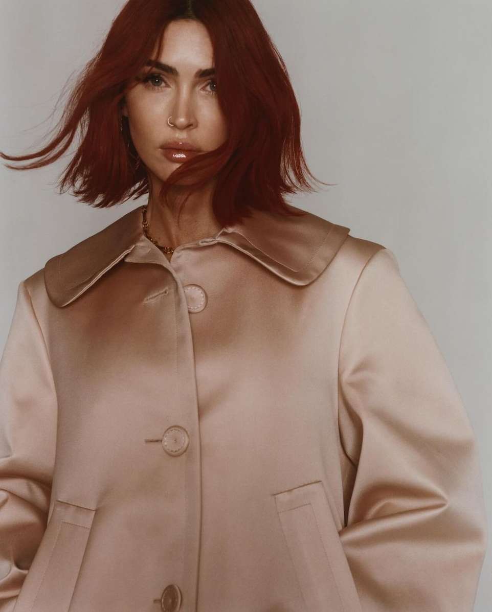 Close-up portrait of a red-haired woman in a pale pink jacket against a neutral backdrop, showcasing a blend of fashion and beauty.