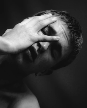 Close-up black and white portrait of a person with short hair holding a hand across their face by photographer Yana Yatsuk.