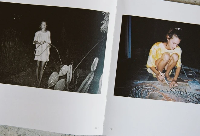 Book spread with an adult female watering plants in a dark garden, and another female working on art in an indoor, low-light setting.