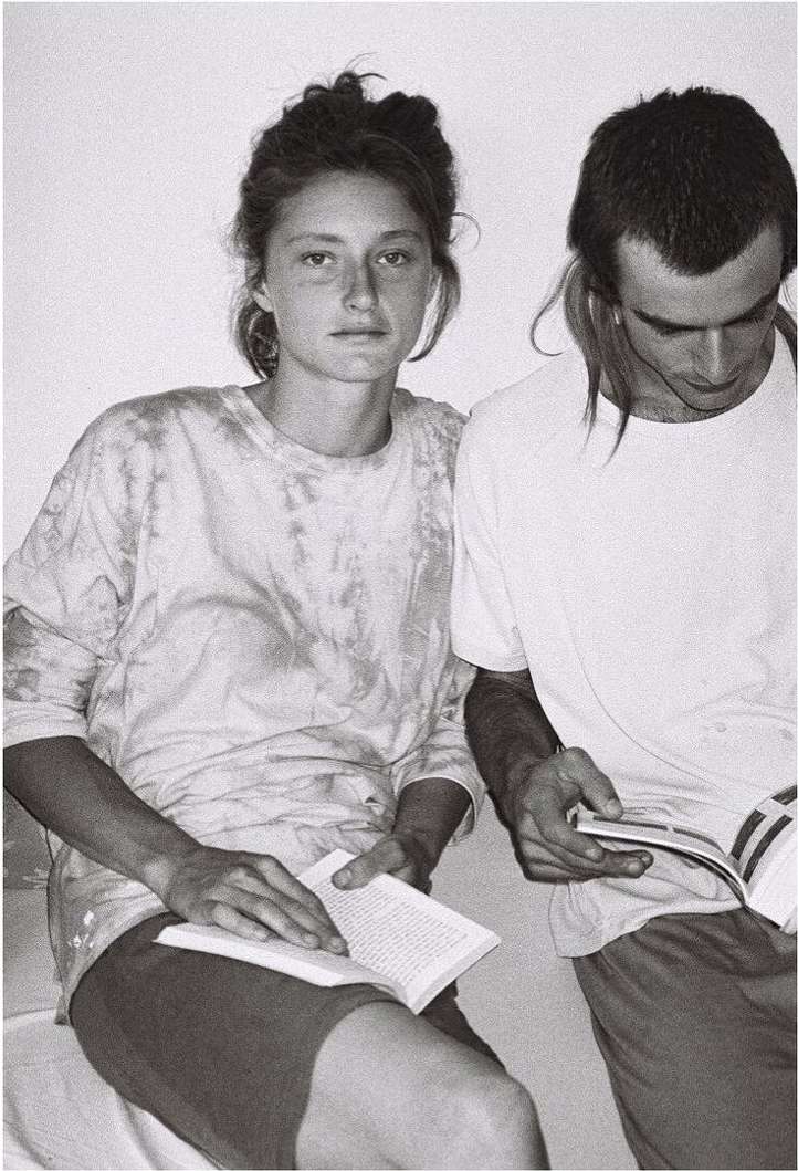 Black and white photograph of a Caucasian woman and man sitting indoors while reading books, facing the camera in casual clothing.