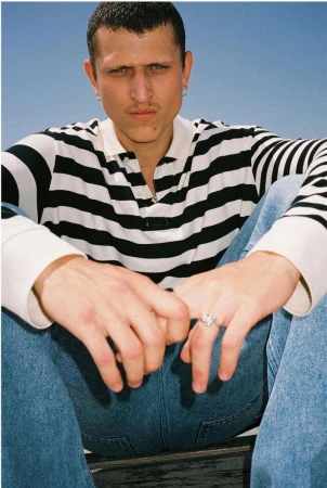 Close-up portrait of a man wearing a black and white striped polo shirt and blue jeans against a clear blue sky.