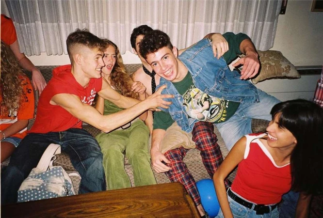 Group of young adults posing indoors, featuring a mix of casual clothing, a blue balloon, and a relaxed, candid atmosphere.
