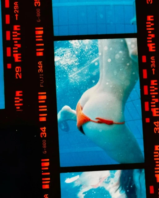 Underwater view of an adult female swimmer in an orange bikini, captured on film, showcasing the subject's back and lower body.
