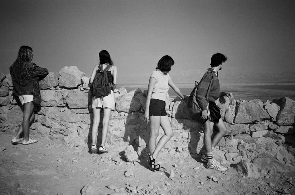 Four people stand on a stone wall overlooking a landscape in a black and white photograph taken at eye-level on a bright, clear day.
