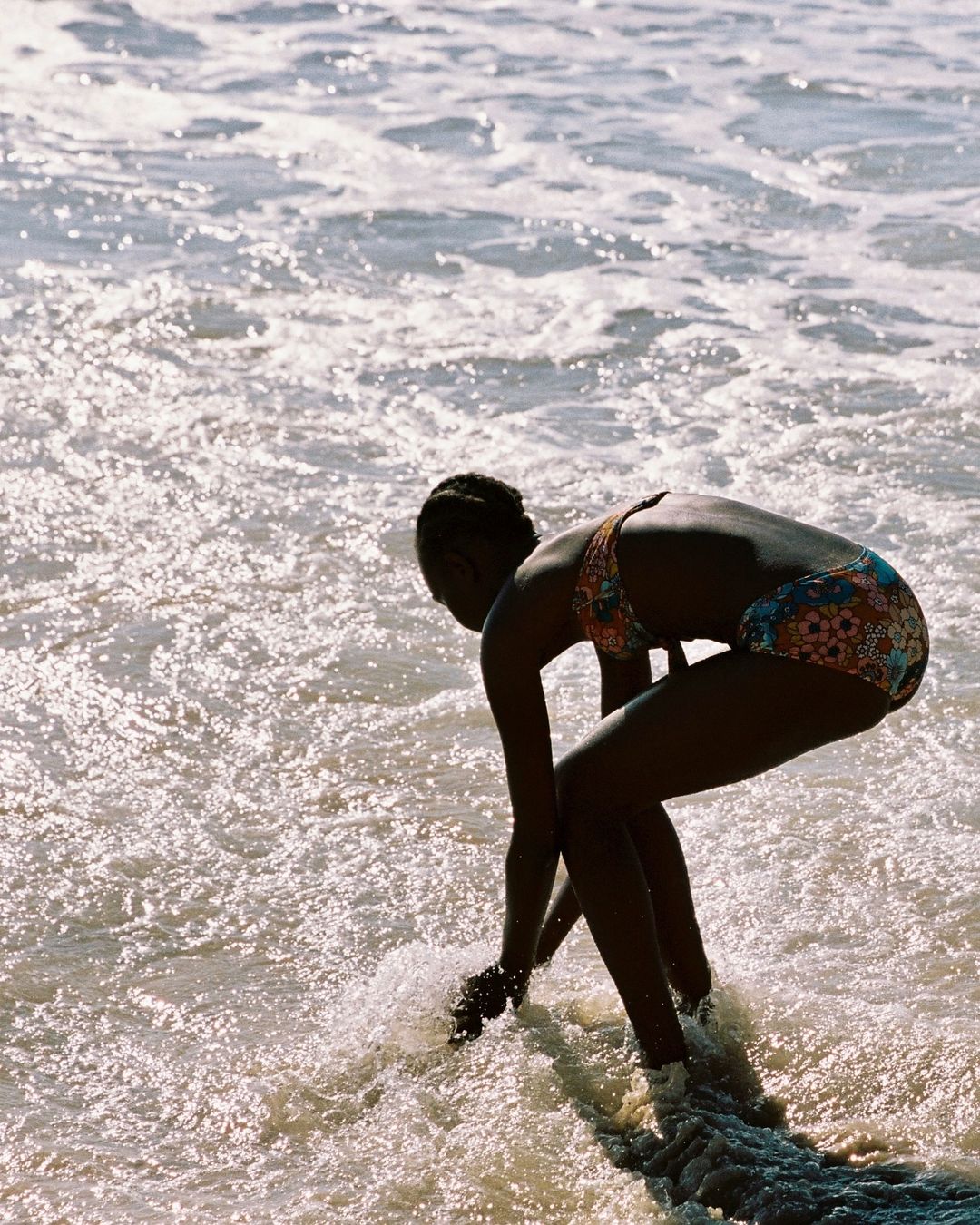 Woman in swimsuit standing in ocean waves on a sunny day, enjoying the water and beach.