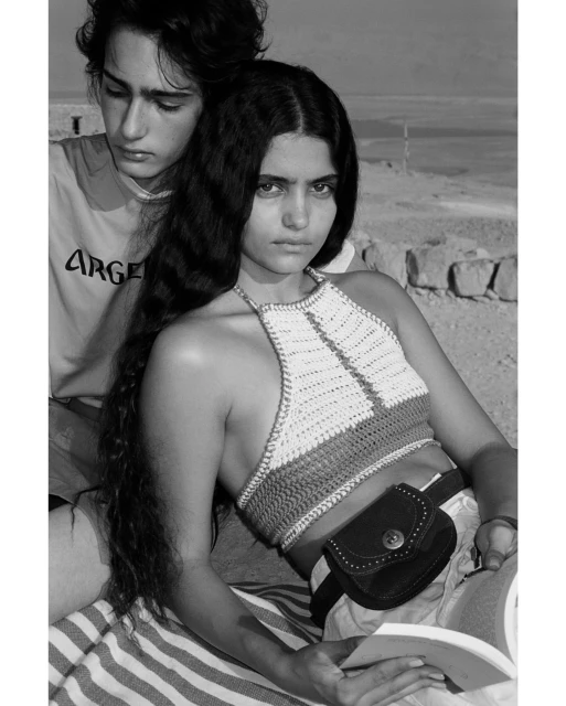 Black and white shot of a young woman in a crocheted halter top and a young man in a tee shirt in an outdoor desert setting.
