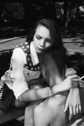 Monochrome portrait of a young woman hugging a shirtless person holding a lit cigarette, captured by Yaniv Edry.