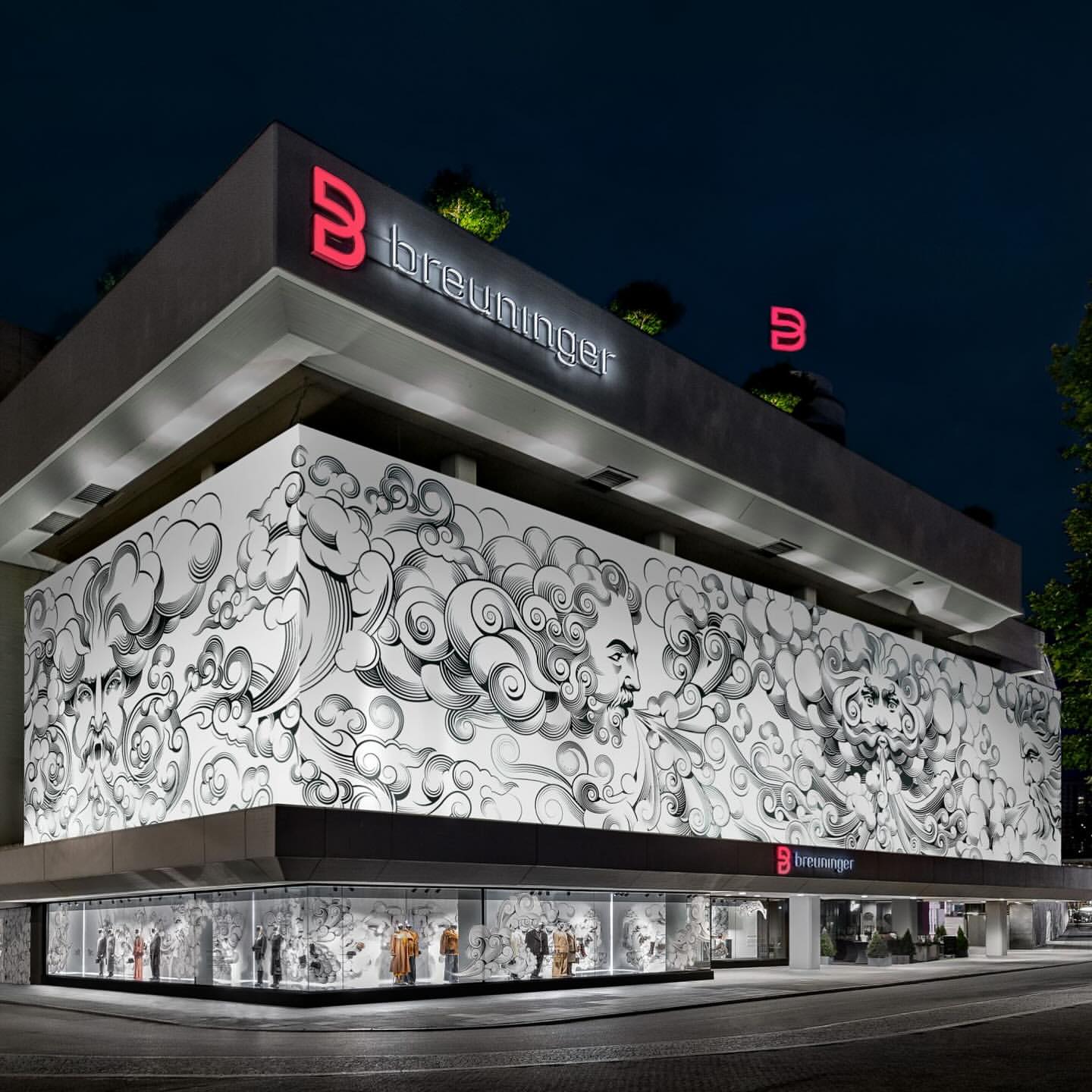 Exterior of Breuninger store at night featuring a large black-and-white mural and illuminated signage with the brand logo.