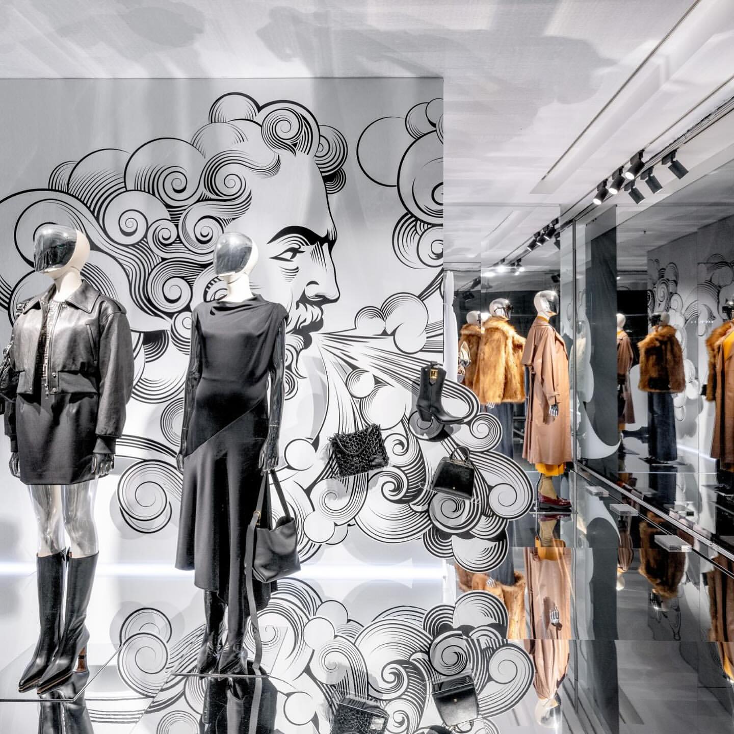 Elegant fashion display with mannequins in dark clothing, handbags, and an artistic backdrop featuring a graphic illustration.