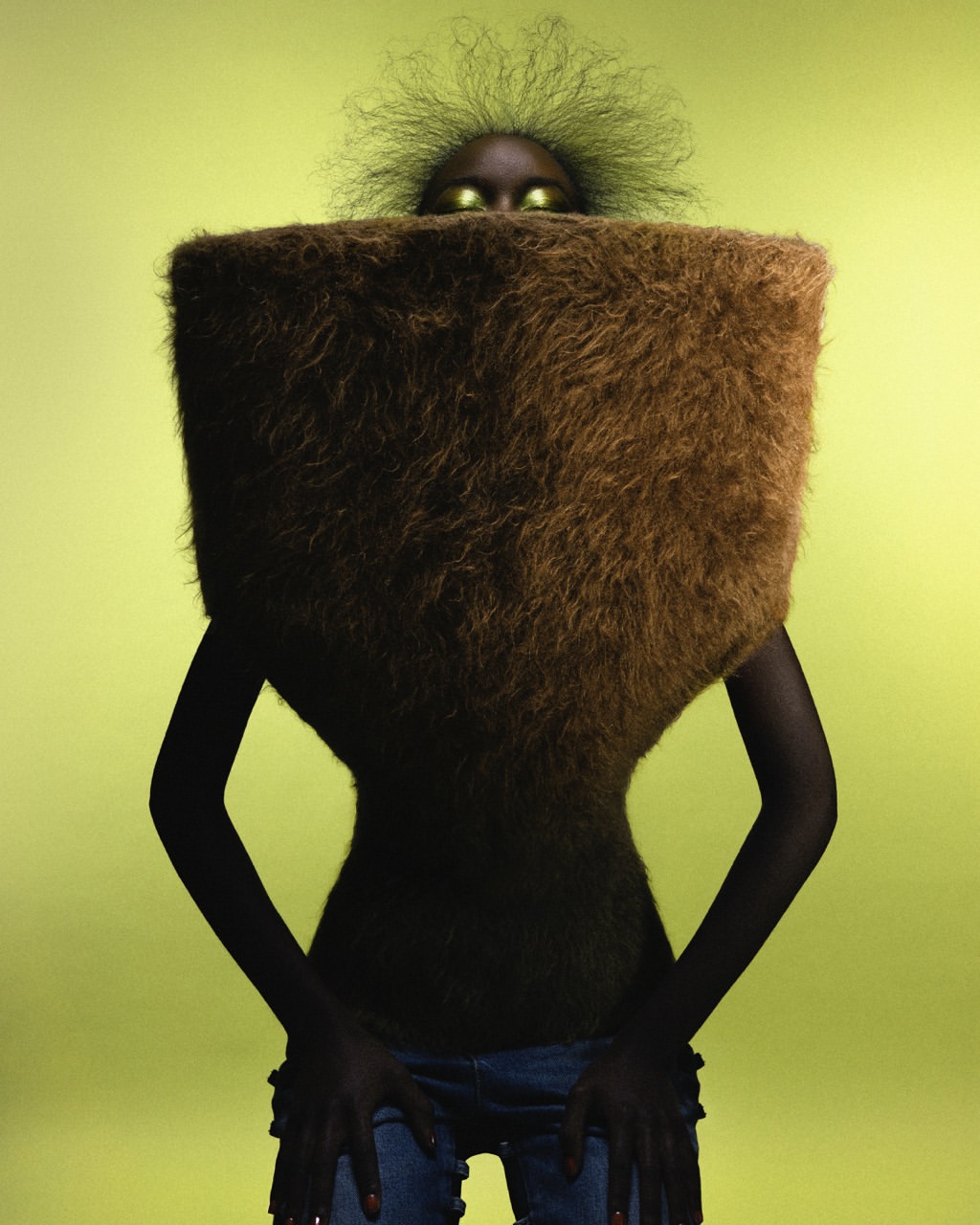 Model with avant-garde fur-like square shawl and Afro hairstyle poses in front of a bright green background in a studio fashion shot.