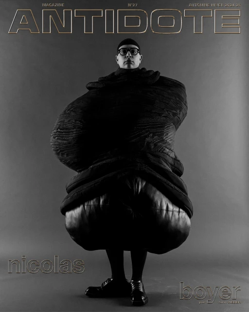 Magazine cover featuring a person wearing black clothing and round eyeglasses, with 'Antidote' magazine title above on a grey background.