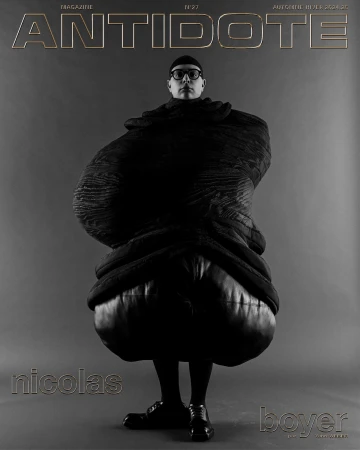 Magazine cover featuring a person wearing black clothing and round eyeglasses, with 'Antidote' magazine title above on a grey background.