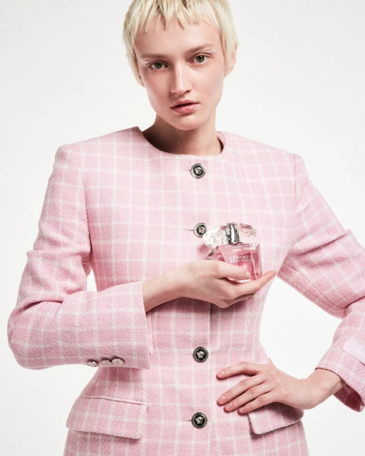 Portrait of a woman in a pink tweed suit holding a pink perfume bottle against a white background in a beauty and fashion setting.