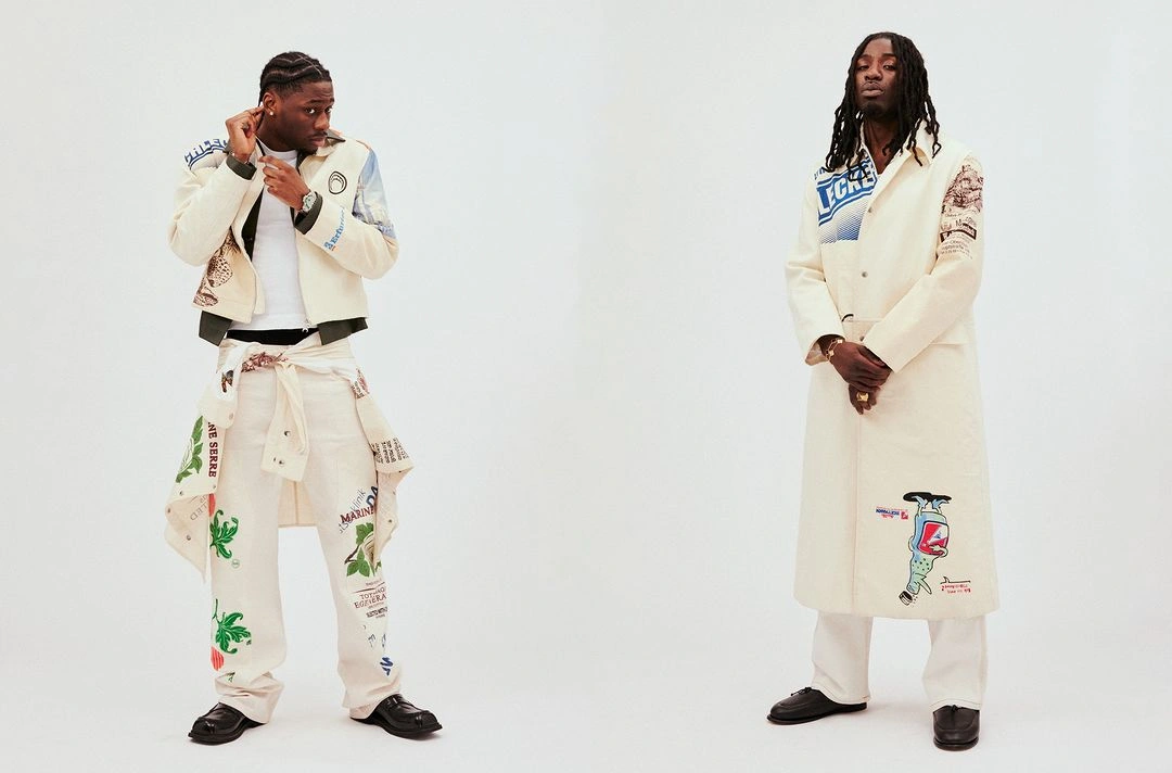 Two black men posing against a white background, wearing cream-colored graphic print jackets and trousers.