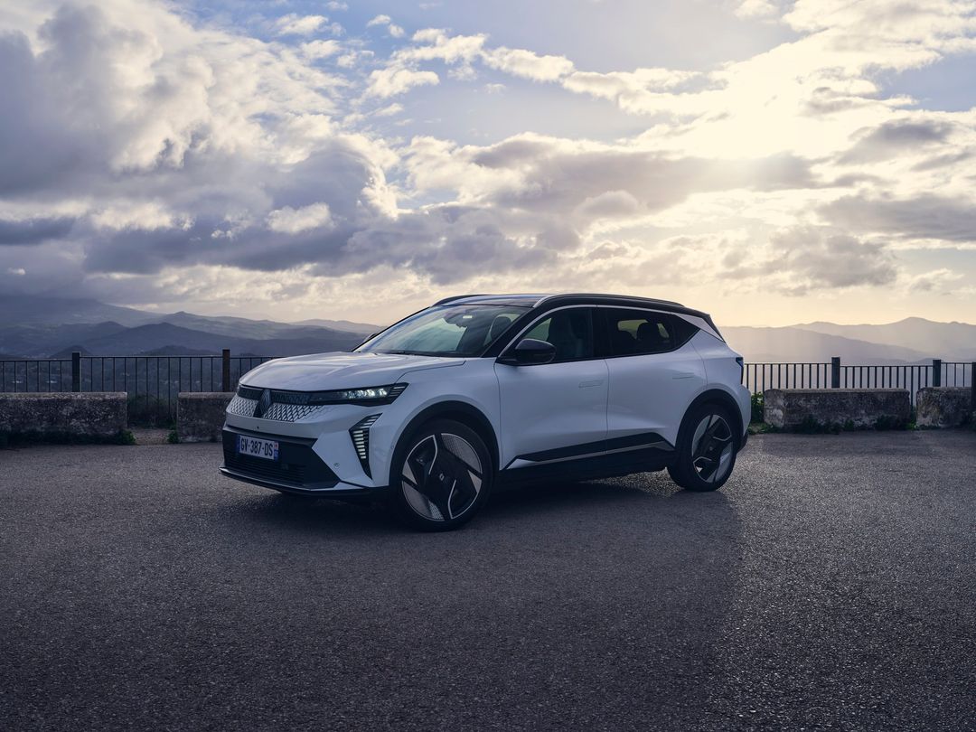 White Renault Rafale E-Tech SUV parked on asphalt road with cloudy skies and a scenic mountain view in the background.