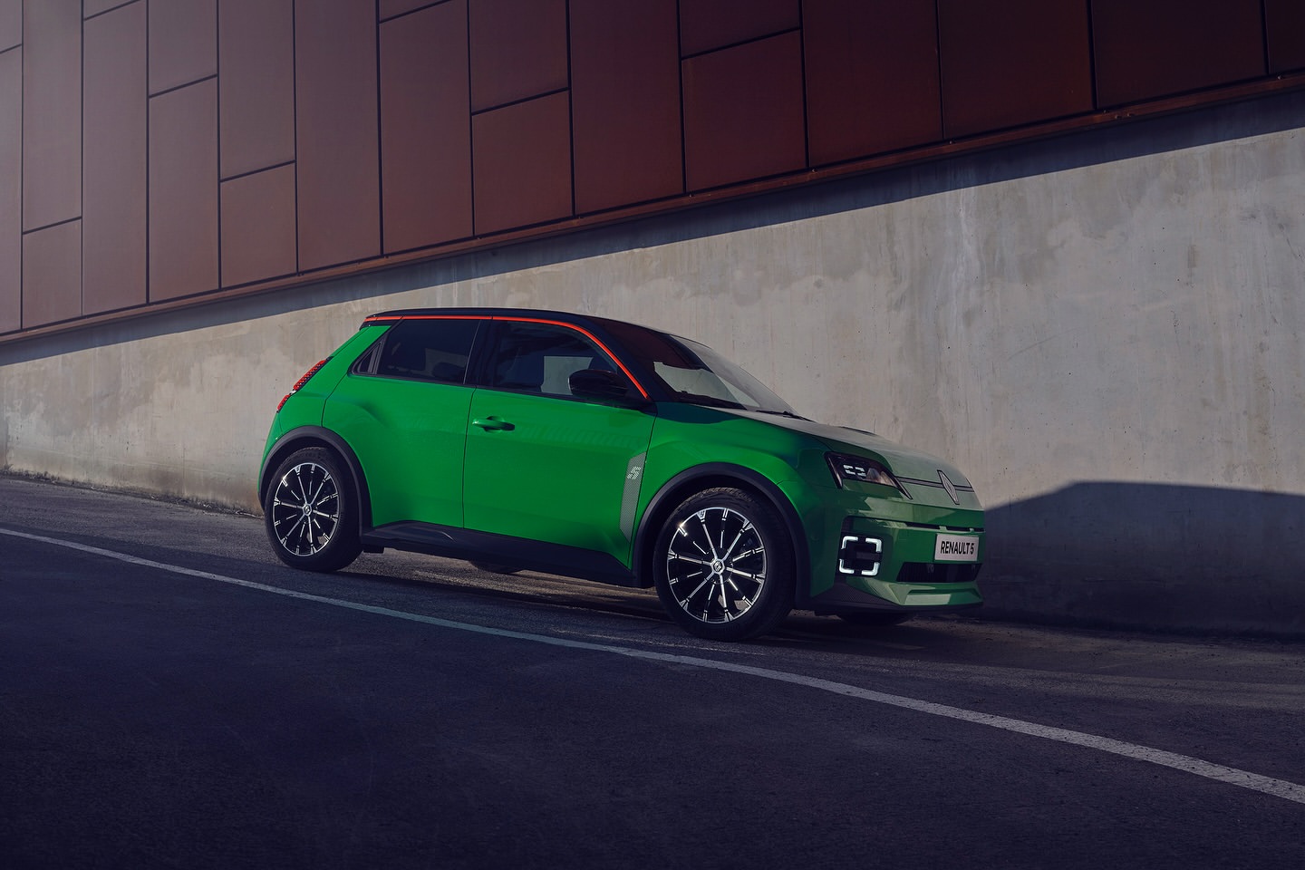 Vibrant green Renault 5 electric car parked on asphalt with modern architecture background, showcasing automotive design and city environment.