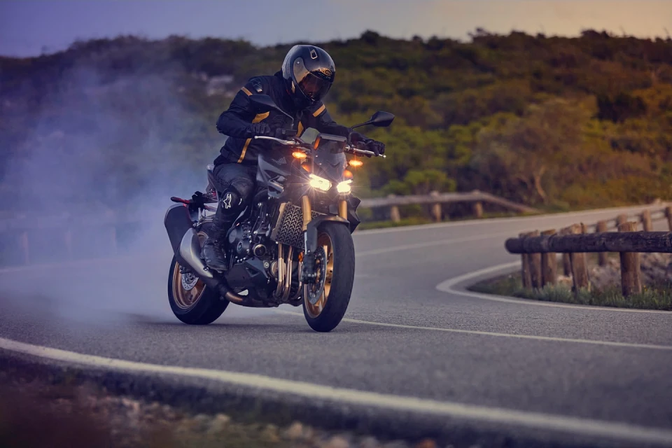 Man riding a black motorcycle on a winding road with green hills at dusk, creating a dynamic image of speed and adventure.