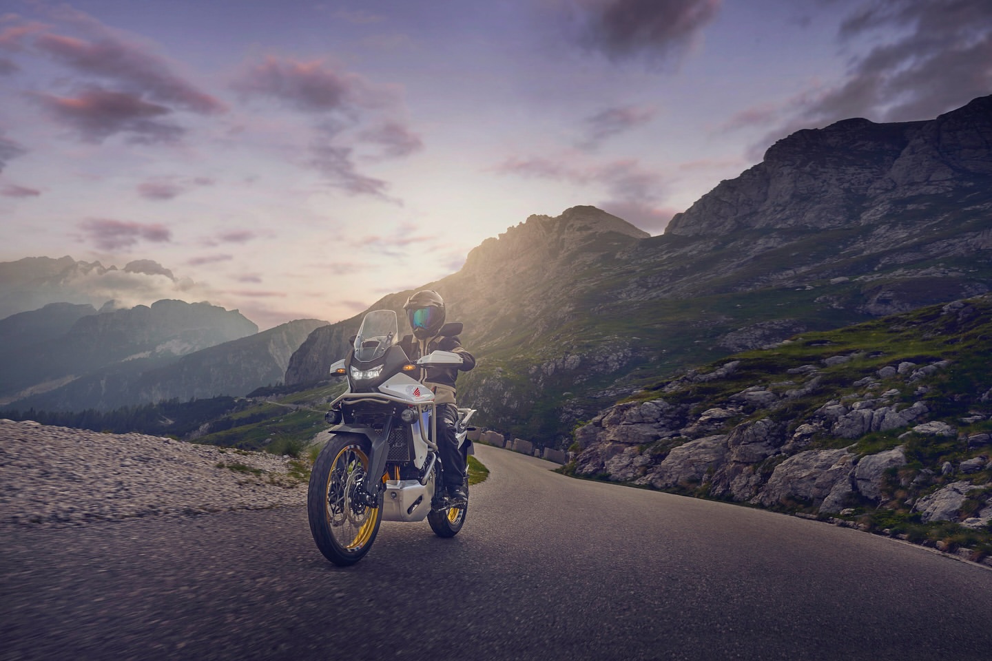Motorcycle rider navigates a winding road through mountainous terrain at dusk, featuring scenic views and adventure riding.