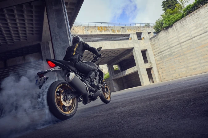 Motorcyclist wearing dark clothing and helmet performs a burnout on a motorcycle on a concrete urban road leaving a smoke trail.