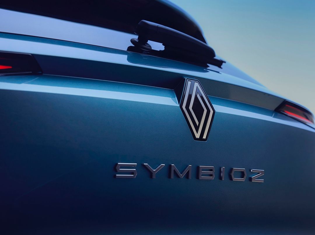 Close-up of a teal Renault Symbioz car, highlighting the brand's logo, rear windshield wiper, and sleek, modern design under natural light.