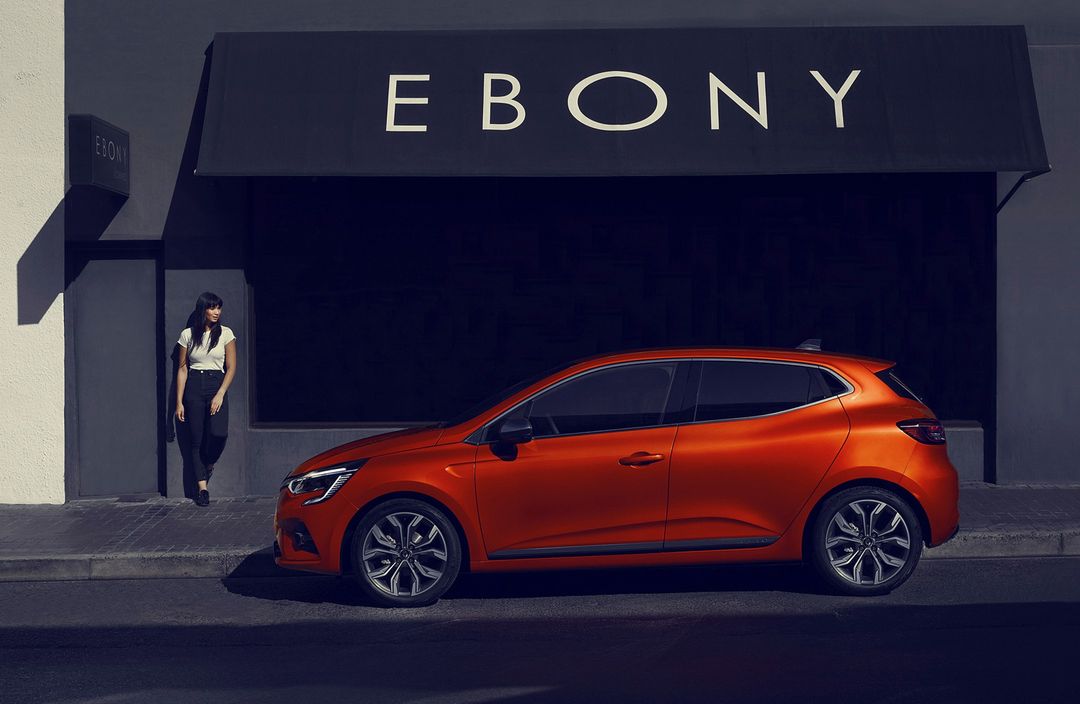 Orange compact car parked on a city street next to a building with 'Ebony' sign; an adult woman walking into the building.