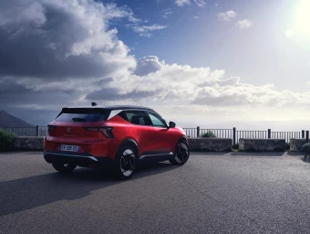 Red electric SUV parked on an asphalt viewpoint overlooking a cloudy coastal landscape by Yannick Brossard.