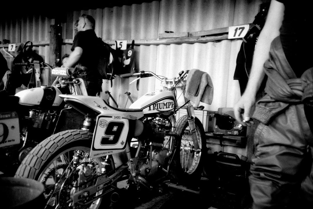 A black and white photograph featuring a Triumph motorcycle with the number 9 displayed on its side in an indoor garage or workshop setting.