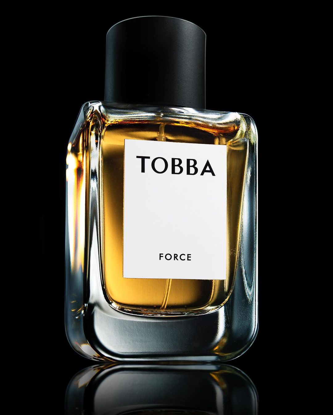Close-up product shot of a Tobba Force perfume bottle with amber liquid against a dark black background