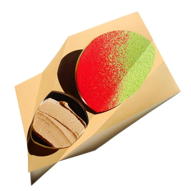 Overhead studio shot of two makeup compacts, one with beige cream and one with red and green powder, against a gold background.