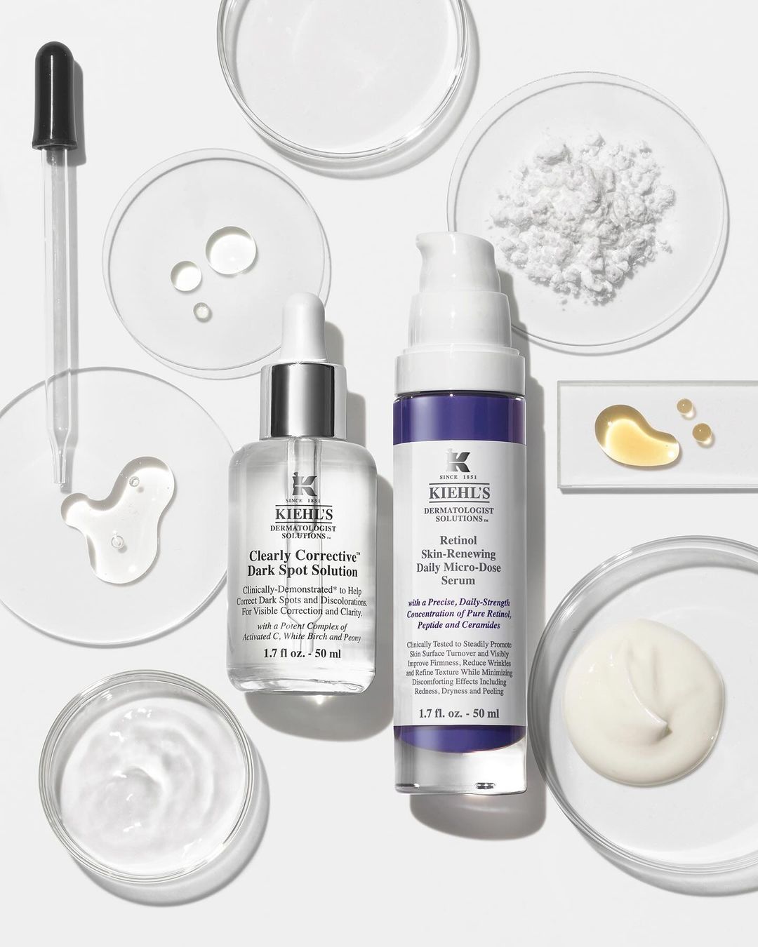 Kiehl's skincare products, including serums and solutions for dark spots and skin renewal, arranged with droppers and laboratory dishes on white.