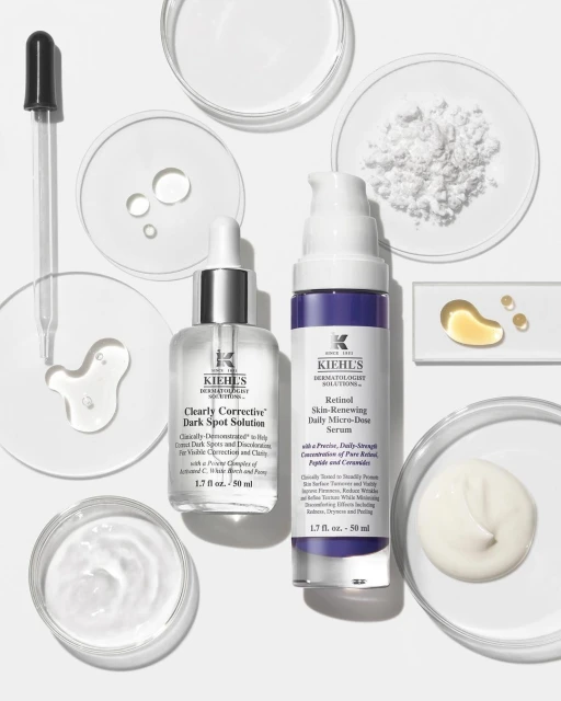 Kiehl's skincare products, including serums and solutions for dark spots and skin renewal, arranged with droppers and laboratory dishes on white.