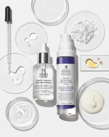 Kiehl's skincare products, including serums and solutions for dark spots and skin renewal, arranged with droppers and laboratory dishes on white.