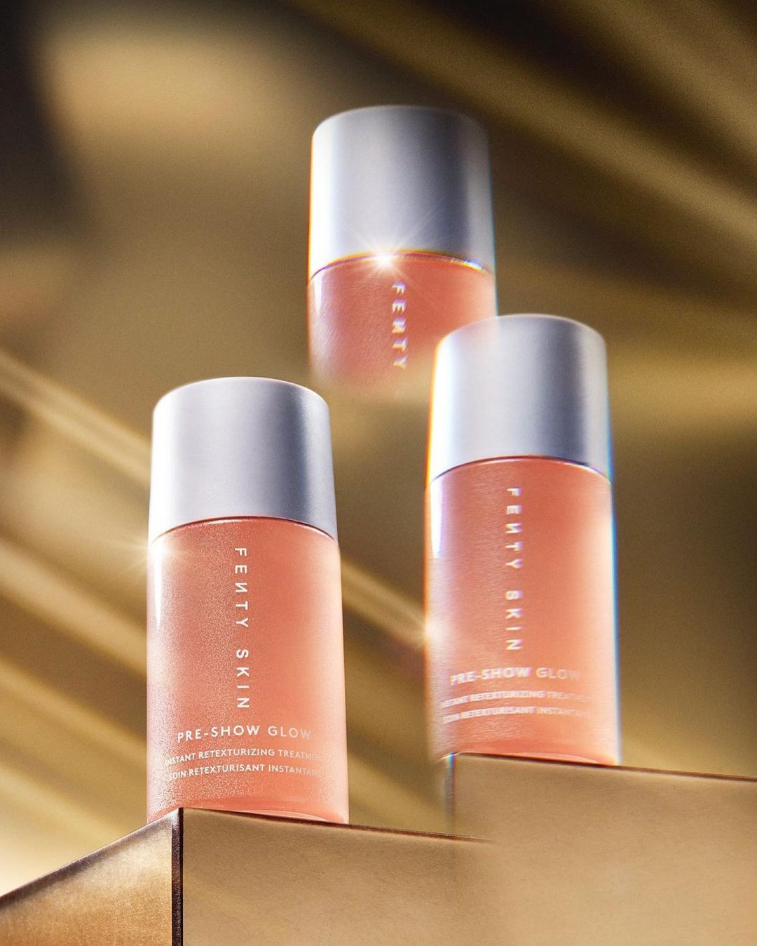 Three Fenty Skin Pre-Show Glow skin treatment bottles on a gold surface with a soft golden background, showcasing a beauty product.