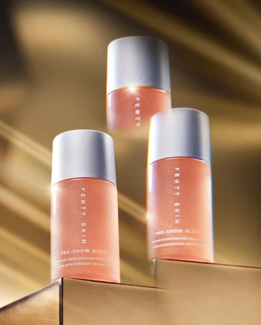 Three Fenty Skin Pre-Show Glow skin treatment bottles on a gold surface with a soft golden background, showcasing a beauty product.