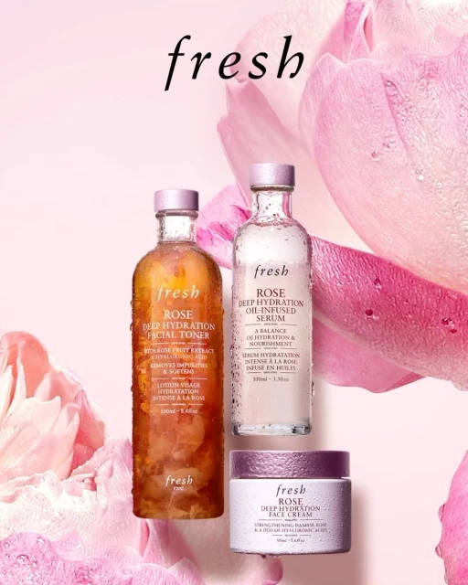 Three Fresh brand skincare bottles are displayed against a blurred pink rose background, featuring facial toner, oil-infused serum, and face cream.