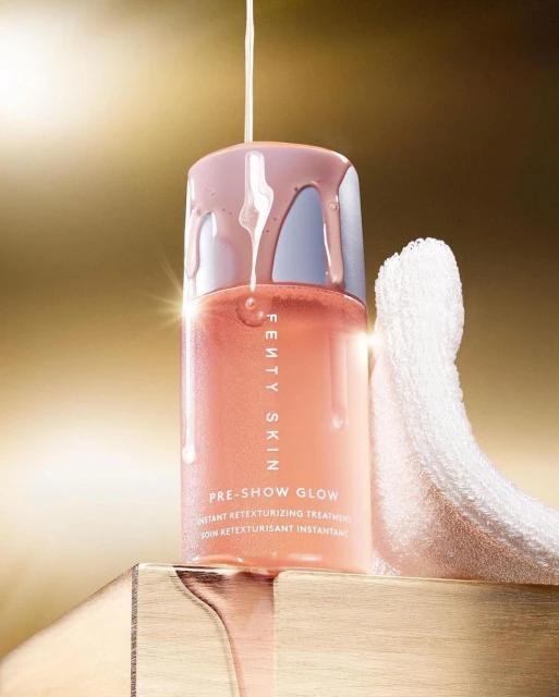 Fenty Skin skincare product shot in studio with golden background and product liquid dripping, focus on the brand's Pre-Show Glow.
