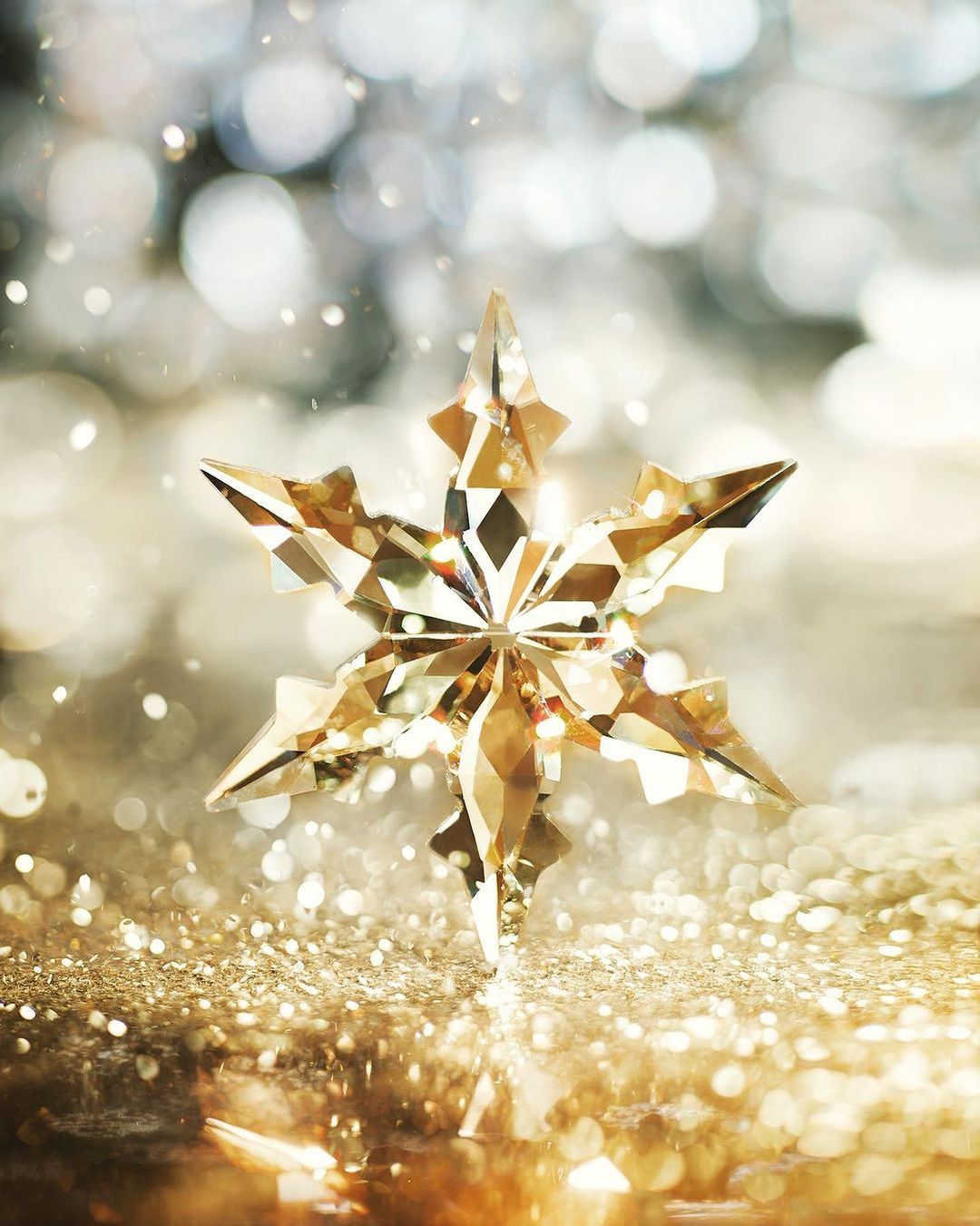 Close-up of a golden crystal star ornament on a shimmering surface with blurred bokeh background, creating a festive holiday theme.