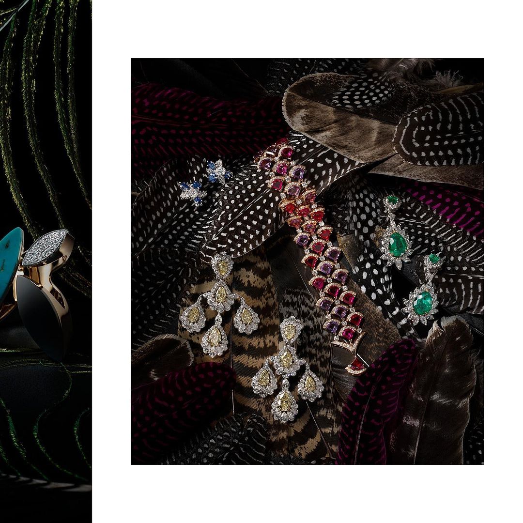 Studio shot of luxury jewelry pieces, including earrings and bracelet, arranged on patterned feathers against a dark background.