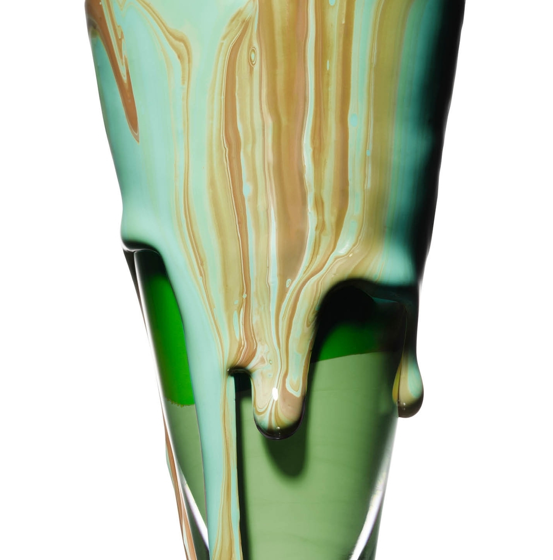 Abstract art of drips in light blue and brown on a green glass vase against white backdrop, showcasing fluid motion and color interplay.