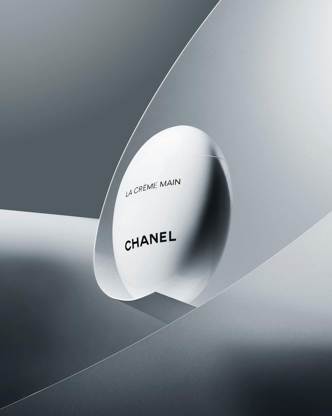 Chanel hand cream product shot. Minimalist composition featuring sleek packaging against a gradient gray backdrop. Beauty and luxury.