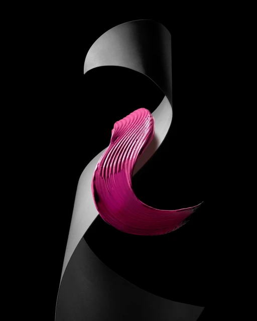 Close-up of a twisted gray paper curl with a stroke of magenta cosmetic product on a stark black background, studio lighting.