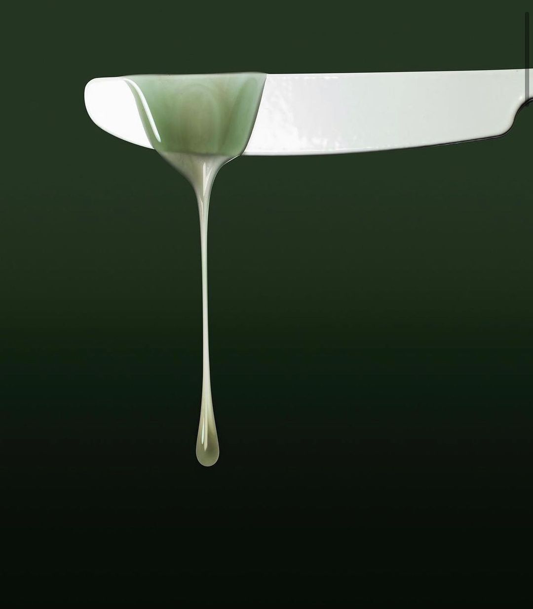 Close-up of white knife with dripping translucent green liquid, studio lighting, dark background; food and beverage concept.