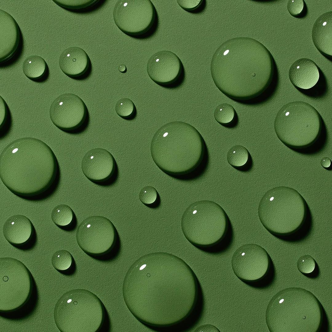 Macro photograph of water droplets of varying sizes scattered across a solid green surface with a soft, diffused light.