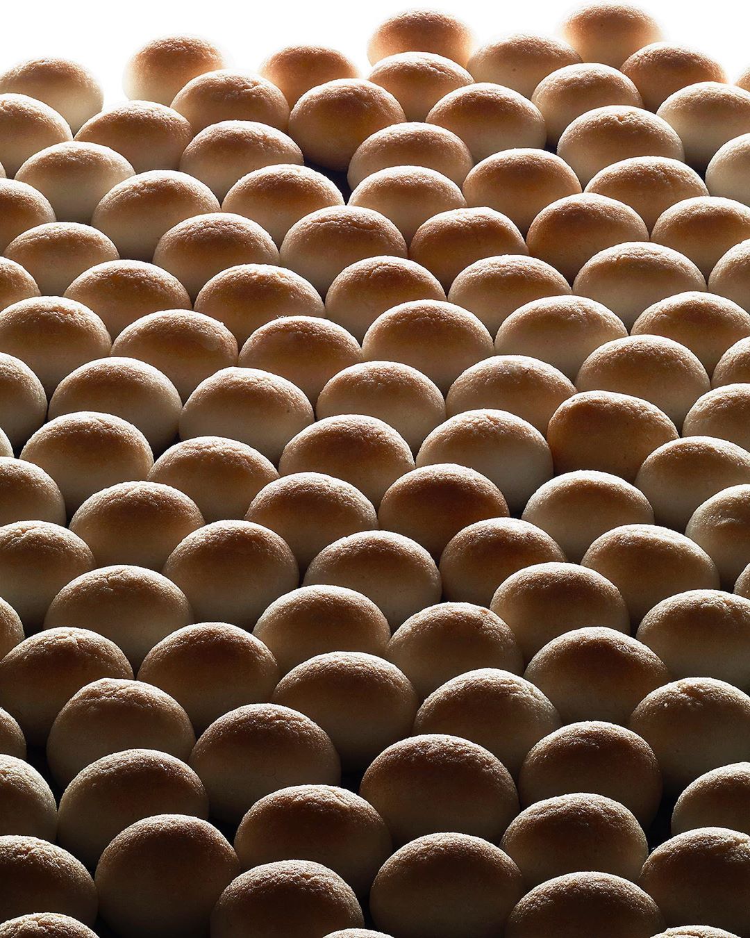 Uniform arrangement of many soft dinner rolls, beautifully backlit with warm light and shadows, creating a visually appealing food pattern.