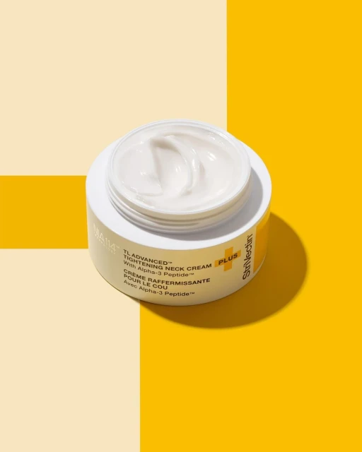 StriVectin TL Advanced Tightening Neck Cream PLUS jar on a yellow and cream-colored background. Focus on skincare and beauty.