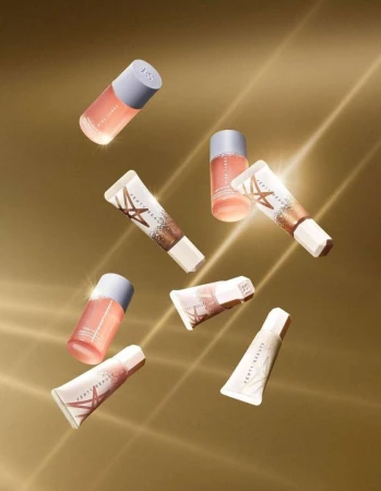 Cosmetic tubes and bottles from Fenty Beauty arranged in a visually appealing pattern against a gold-colored background with light rays.