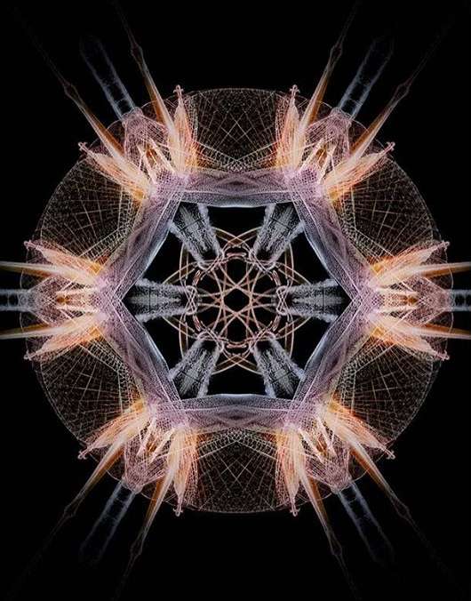 Intricate starburst pattern with radiating lines and geometric shapes in shades of peach, grey, and white against a dark background.