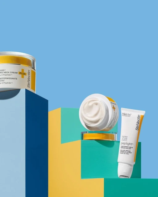 Three skincare products by Strivectin are displayed on colorful geometric steps against a light blue background in a studio product shot.