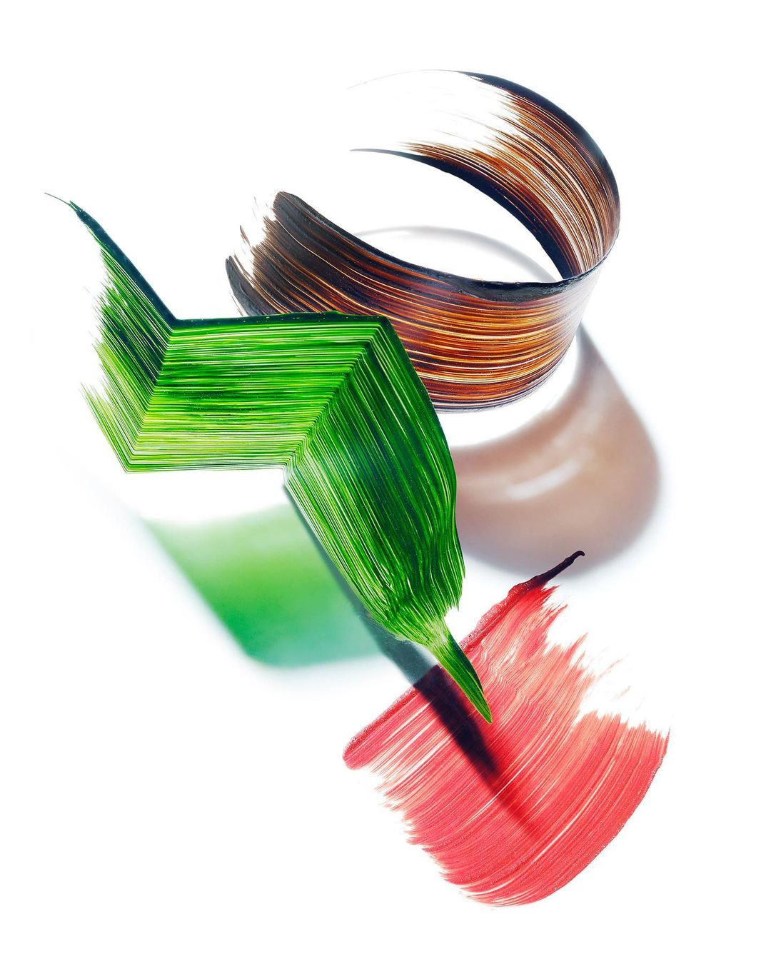 Abstract still life with geometric paper shapes in green, red, and brown hues against a clean white background, creating dynamic color contrast.